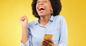 Schwarze Frau hält ein Smartphone in der Hand und freut sich über einen günstigen Handy-Tarif. Bild: iStock-1494508936-Jacob Wackerhausen