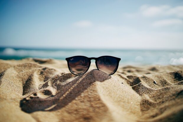 Sonnenbrille im Sand. Urlaub geht auch nachhaltig. Tipps dafür gibt's im Text.